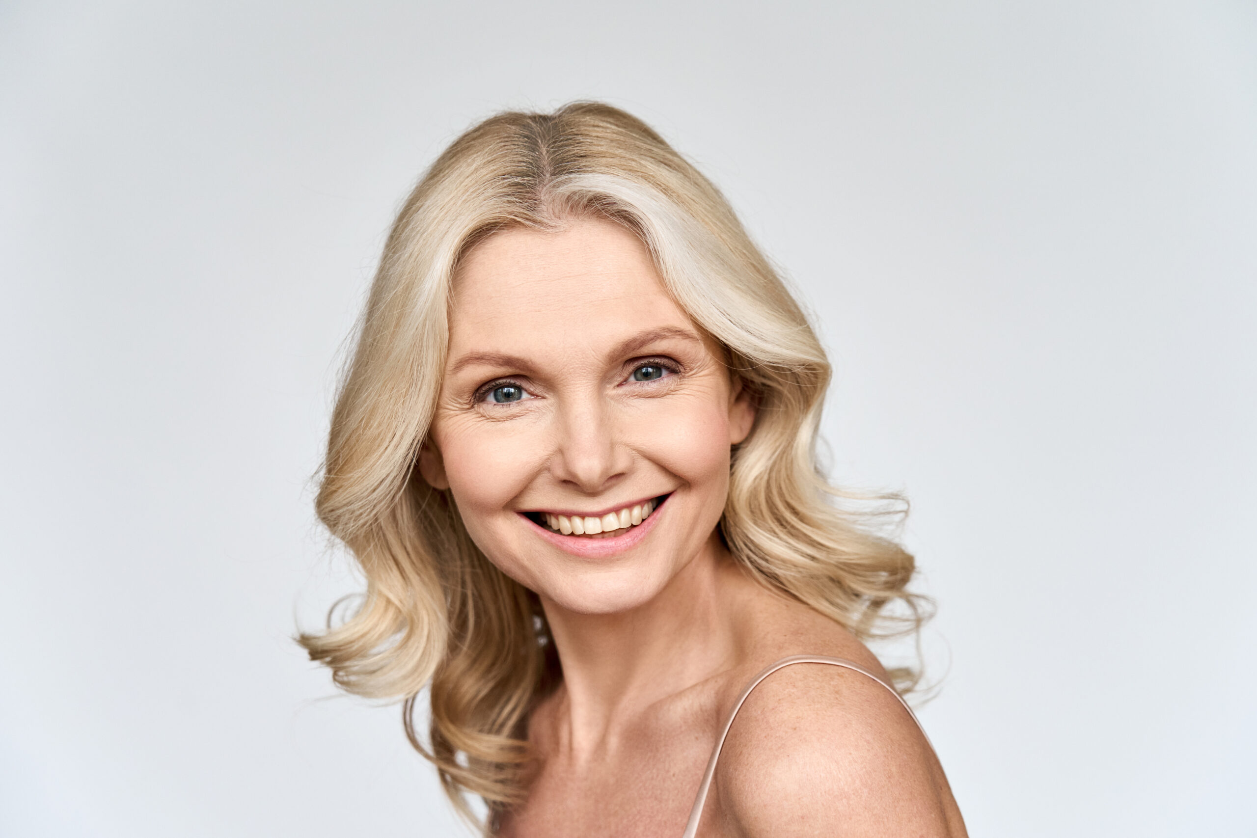 Gorgeous happy smiling middle 50s age woman looking at camera portrait isolated on white background. Face tighten rejuvenating skin care products advertising concept.